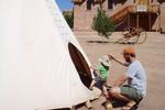 Father helping child to get into a teepee at Bluff Fort